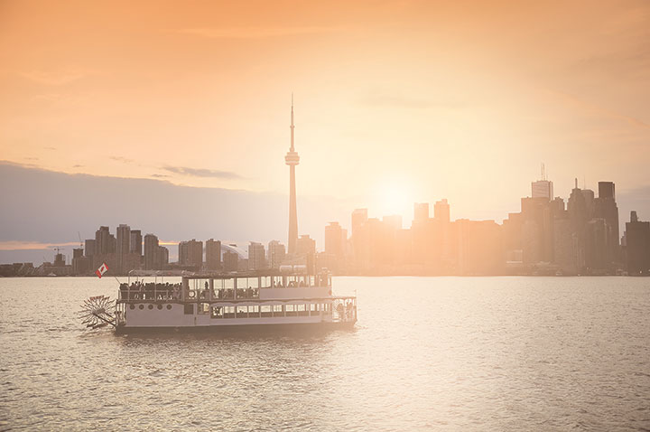 The Toronto Island ferry on the lake with the Toronto skyline and sunset in the background.