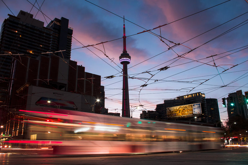 A streetcar passing by the CN Tower during dusk.